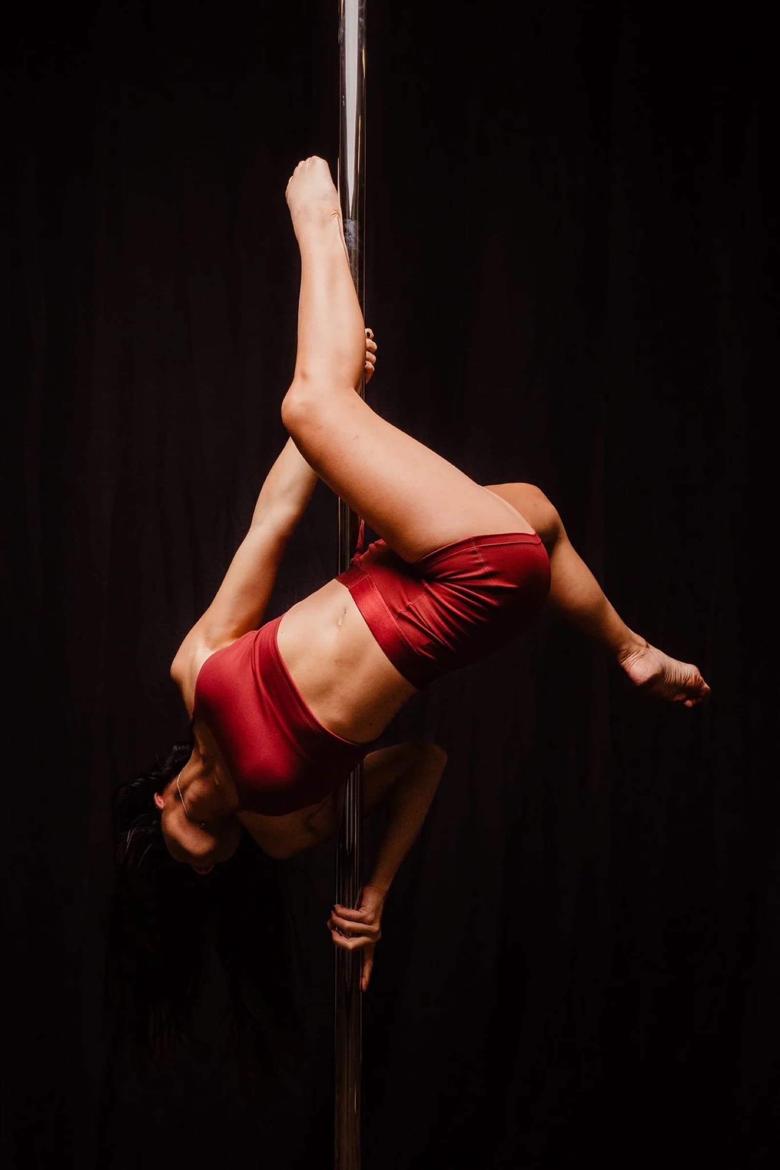 A La Bombe pole performer in red demonstrating a suspended pose